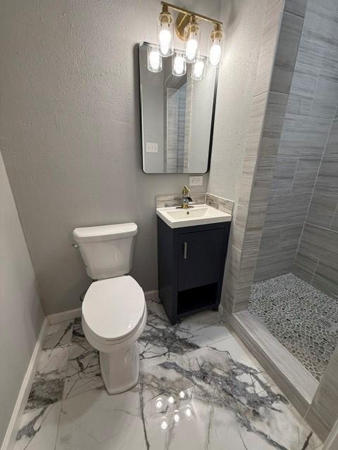 bathroom featuring toilet, a tile shower, and vanity