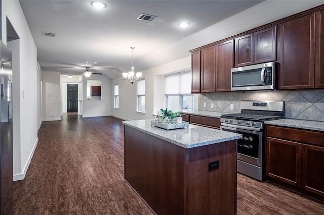 kitchen featuring ceiling fan with notable chandelier, light stone countertops, appliances with stainless steel finishes, a kitchen island, and backsplash