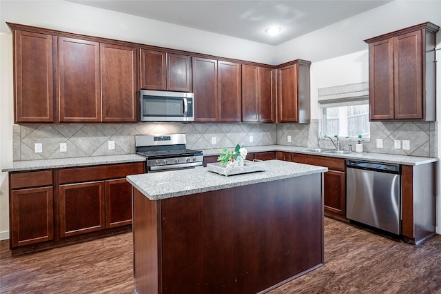 kitchen with appliances with stainless steel finishes, a kitchen island, dark hardwood / wood-style flooring, sink, and light stone counters