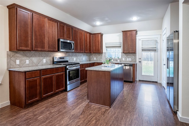 2418 San Marcos Dr, Forney, TX 75126 - kitchen with dark wood finished floors, light stone counters, stainless steel appliances, a center island, and decorative backsplash