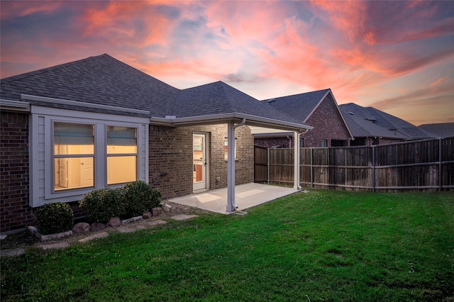 back house at dusk with a patio area and a yard