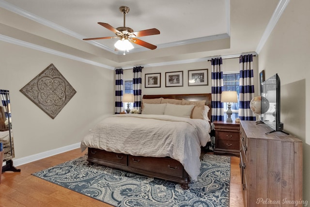 bedroom with ceiling fan, a raised ceiling, light wood-type flooring, and ornamental molding