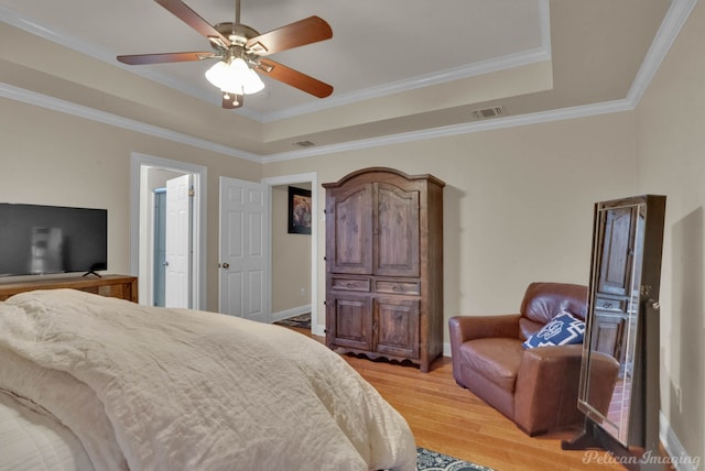 bedroom featuring ceiling fan, a raised ceiling, crown molding, and light hardwood / wood-style flooring