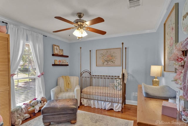 bedroom featuring ceiling fan, hardwood / wood-style floors, a crib, and ornamental molding