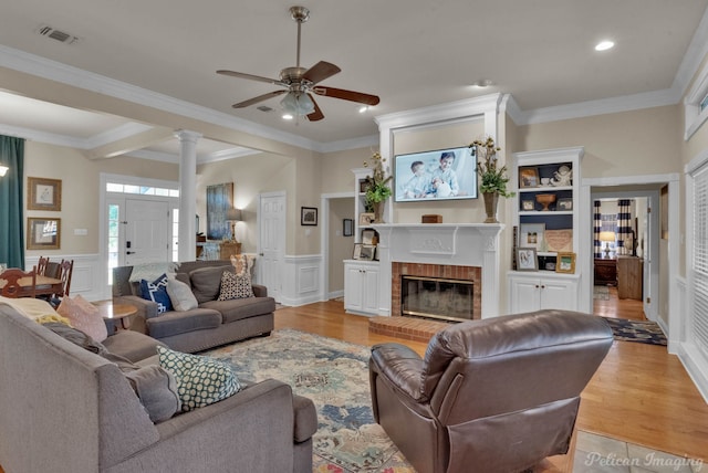 living room with ornate columns, ornamental molding, ceiling fan, light hardwood / wood-style flooring, and a fireplace