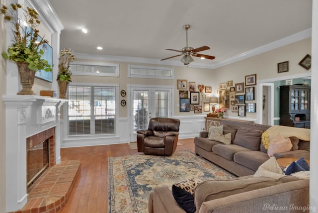 living room featuring french doors, ornamental molding, ceiling fan, a fireplace, and light hardwood / wood-style floors