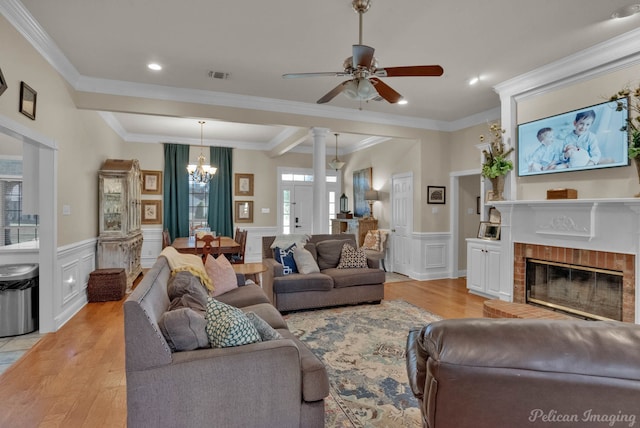 living room with decorative columns, ceiling fan with notable chandelier, crown molding, light hardwood / wood-style flooring, and a fireplace