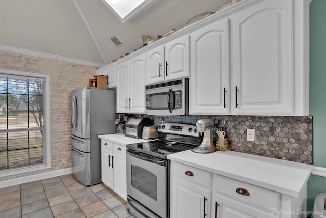 kitchen with ornamental molding, stainless steel appliances, vaulted ceiling, light tile patterned floors, and white cabinetry