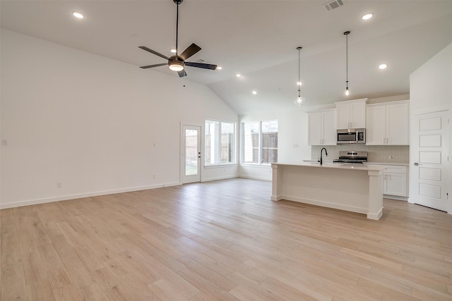 kitchen with a center island with sink, white cabinetry, stainless steel appliances, and light wood-type flooring