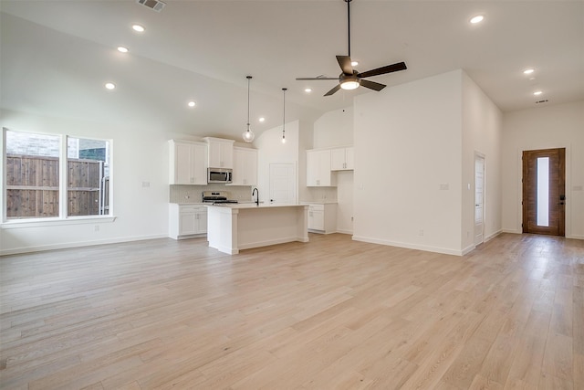 kitchen with white cabinets, a kitchen island with sink, high vaulted ceiling, light wood-type flooring, and stainless steel appliances