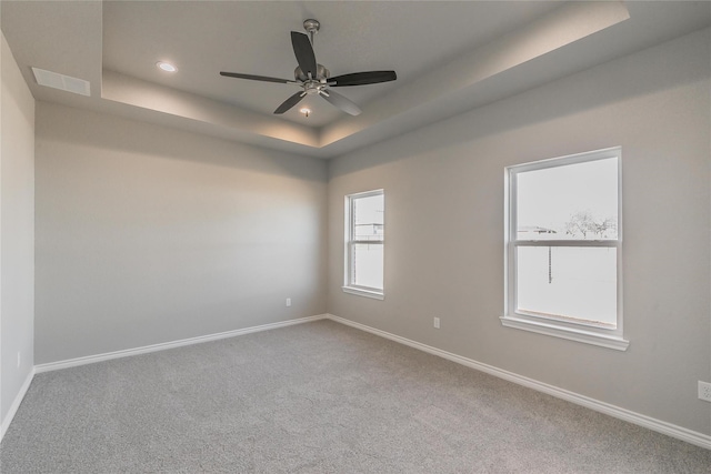 empty room with a tray ceiling, carpet, and ceiling fan