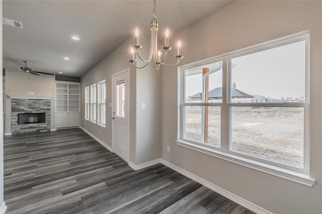 interior space with dark wood-type flooring, a tiled fireplace, built in features, and ceiling fan with notable chandelier