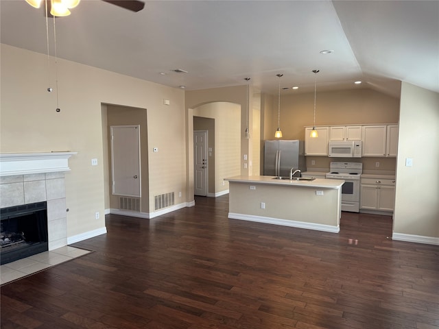 kitchen with white appliances, a tiled fireplace, dark wood-type flooring, and an island with sink