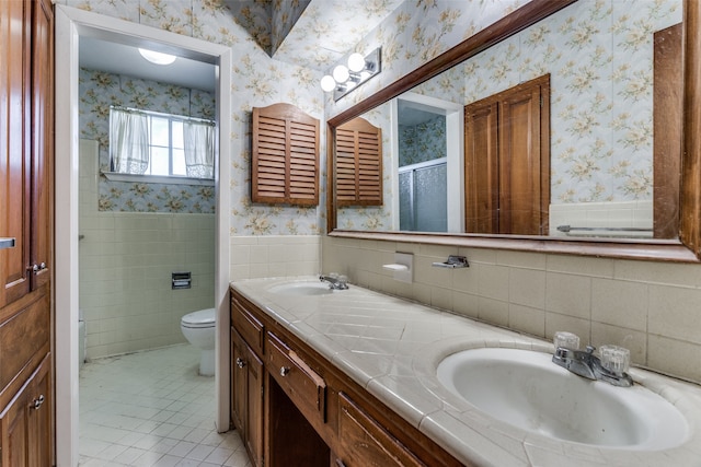 bathroom with a shower with shower door, toilet, tile patterned floors, tile walls, and vanity