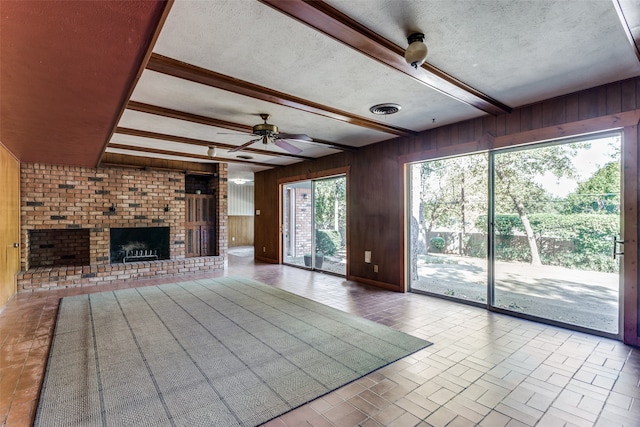 unfurnished living room featuring wood walls, a textured ceiling, a wealth of natural light, and a fireplace