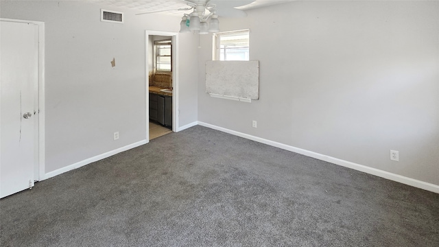 unfurnished bedroom with dark colored carpet, ensuite bath, and ceiling fan