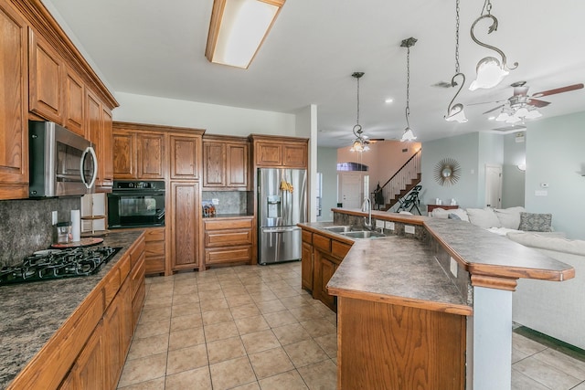 kitchen with sink, backsplash, pendant lighting, a kitchen island with sink, and black appliances