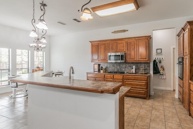 kitchen featuring a notable chandelier, pendant lighting, a kitchen island with sink, light tile patterned flooring, and black appliances