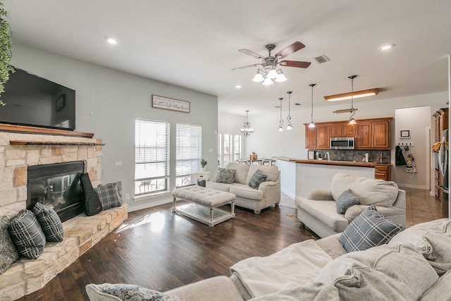 living room with a fireplace, ceiling fan with notable chandelier, and dark wood-type flooring