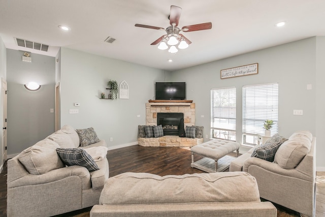 living room with ceiling fan, a stone fireplace, and dark wood-type flooring