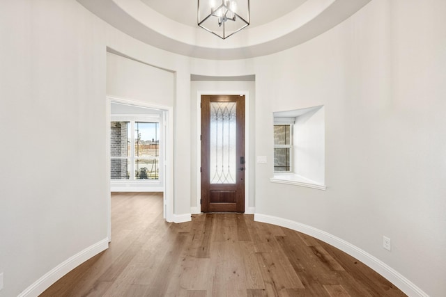 foyer with light wood-type flooring, a raised ceiling, and a notable chandelier