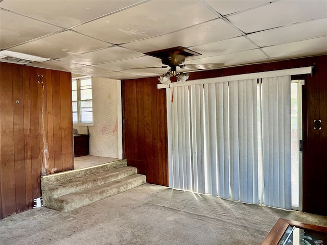 stairs featuring a paneled ceiling, a healthy amount of sunlight, wooden walls, and carpet flooring