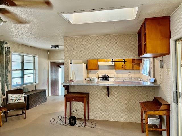 kitchen with white refrigerator, kitchen peninsula, a kitchen bar, range, and a skylight