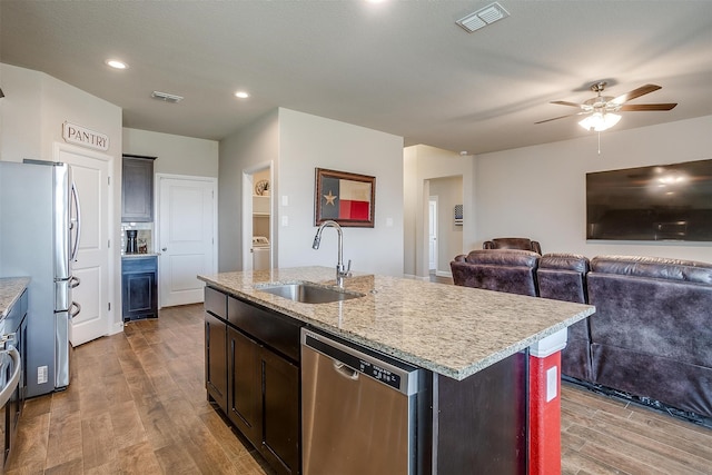 kitchen with ceiling fan, sink, stainless steel appliances, light hardwood / wood-style floors, and a center island with sink