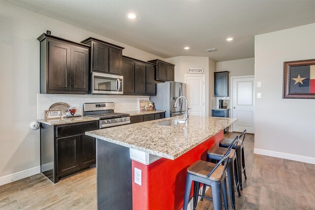 kitchen with a kitchen bar, stainless steel appliances, light hardwood / wood-style flooring, and an island with sink