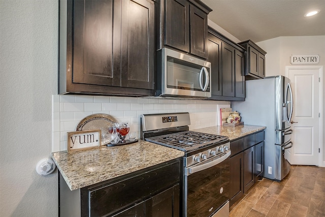 kitchen featuring light wood-type flooring, tasteful backsplash, light stone counters, dark brown cabinetry, and stainless steel appliances