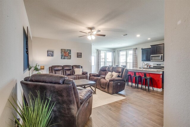 living room featuring ceiling fan, sink, wood-type flooring, and a textured ceiling