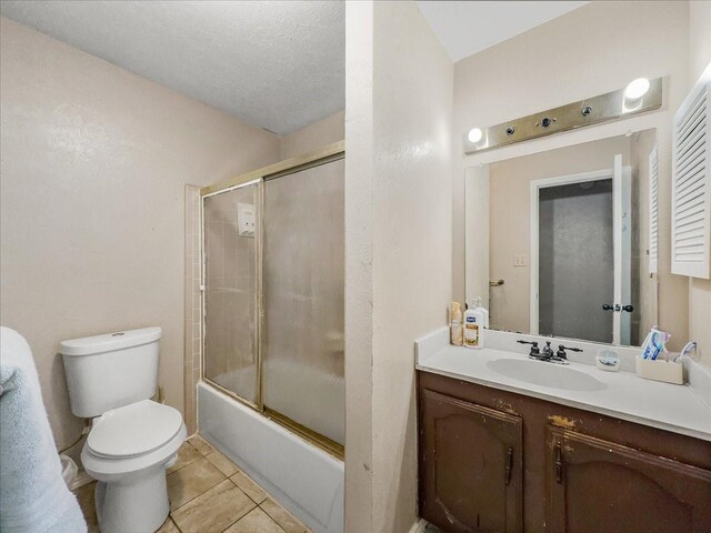 full bathroom with vanity, shower / bath combination with glass door, tile patterned flooring, toilet, and a textured ceiling