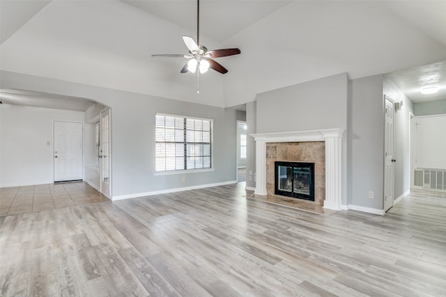 unfurnished living room featuring a tiled fireplace, vaulted ceiling, and light wood-type flooring