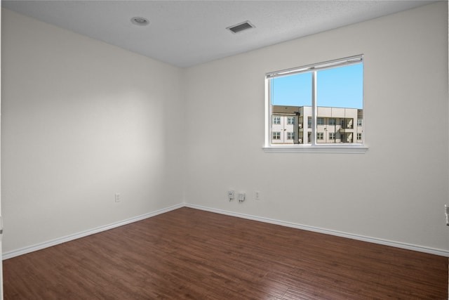 spare room with visible vents, baseboards, and dark wood-style flooring