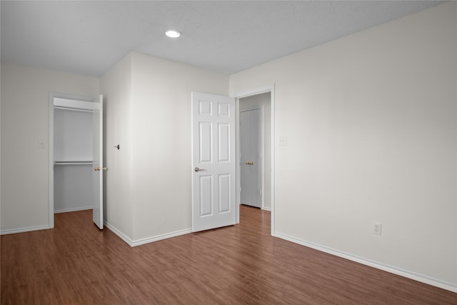 unfurnished bedroom with a closet, baseboards, wood finished floors, and a spacious closet