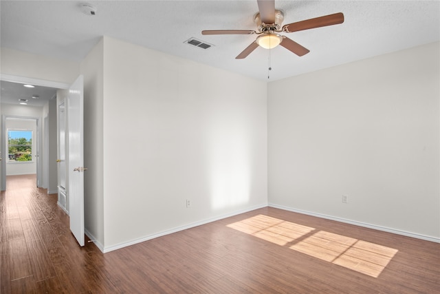 empty room with a ceiling fan, wood finished floors, visible vents, and baseboards