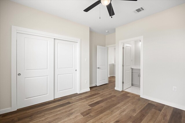 unfurnished bedroom featuring ensuite bath, ceiling fan, a closet, and dark wood-type flooring