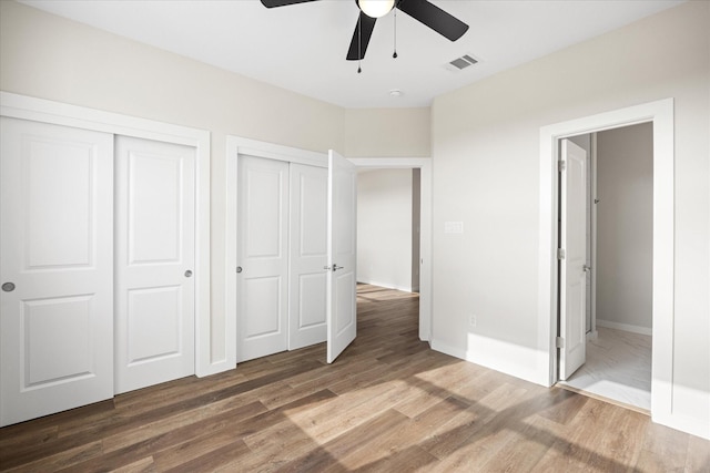 unfurnished bedroom featuring ceiling fan, wood-type flooring, and multiple closets