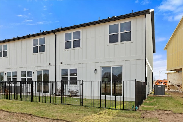 rear view of house with central air condition unit and a lawn