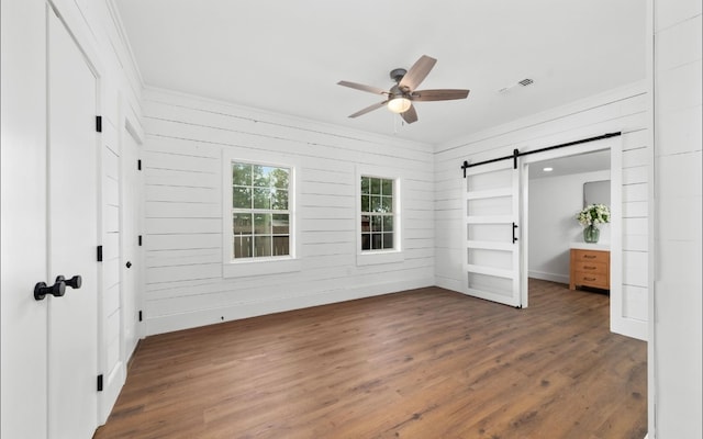 unfurnished bedroom featuring ceiling fan, a barn door, and dark hardwood / wood-style flooring