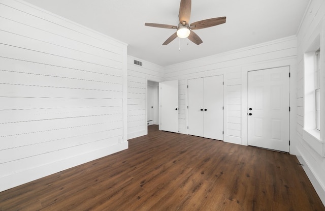 unfurnished bedroom with dark wood-type flooring, ceiling fan, and multiple closets