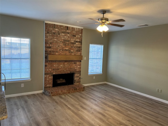 unfurnished living room featuring hardwood / wood-style flooring, ceiling fan, and a brick fireplace