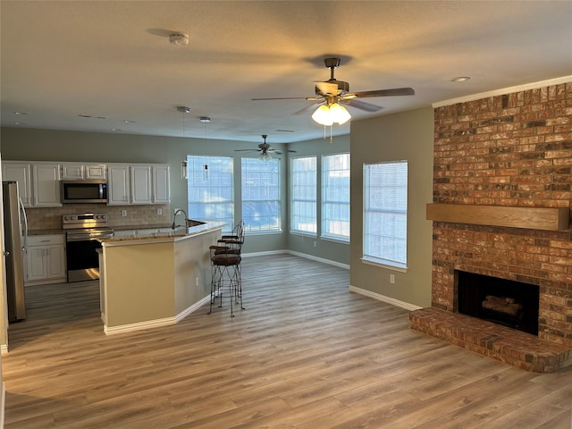 kitchen with appliances with stainless steel finishes, a kitchen bar, a fireplace, white cabinets, and light hardwood / wood-style flooring