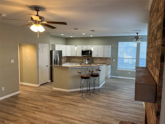 kitchen featuring a kitchen breakfast bar, stainless steel appliances, decorative light fixtures, white cabinets, and light hardwood / wood-style flooring