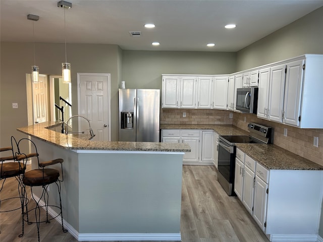 kitchen with appliances with stainless steel finishes, white cabinets, decorative light fixtures, and light hardwood / wood-style floors