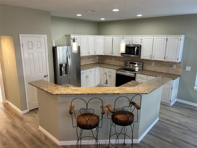 kitchen with light wood-type flooring, backsplash, stainless steel appliances, decorative light fixtures, and white cabinets