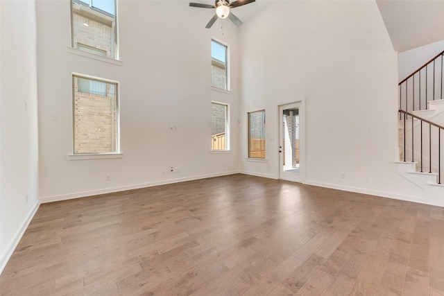 unfurnished living room with a towering ceiling, a ceiling fan, wood finished floors, baseboards, and stairs