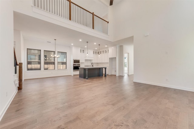 unfurnished living room featuring light wood-type flooring, baseboards, and a notable chandelier