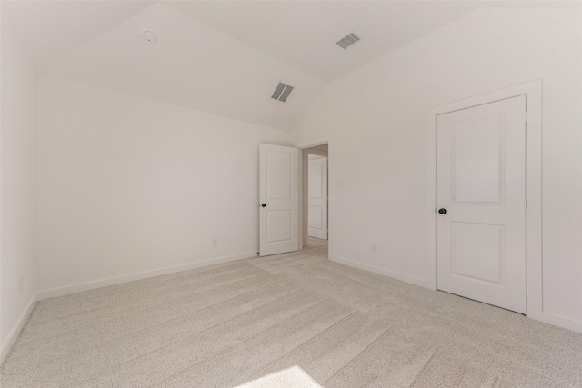 empty room featuring vaulted ceiling, light carpet, visible vents, and baseboards