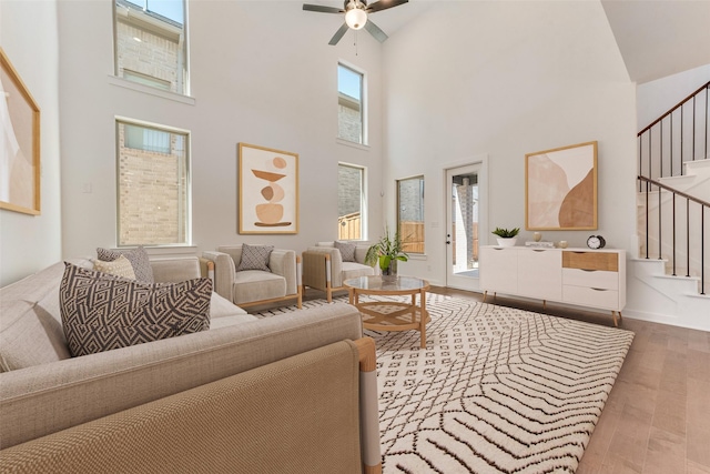 living room with stairs, ceiling fan, a high ceiling, and wood finished floors